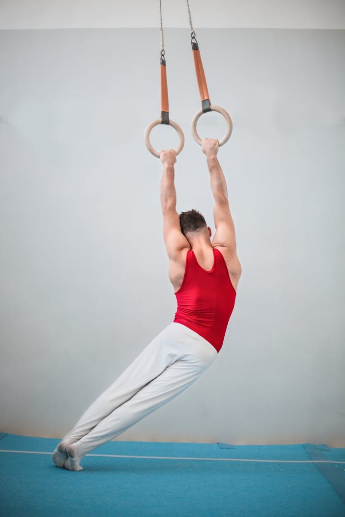 A male gymnast displaying strength and balance on rings inside a gym setting.